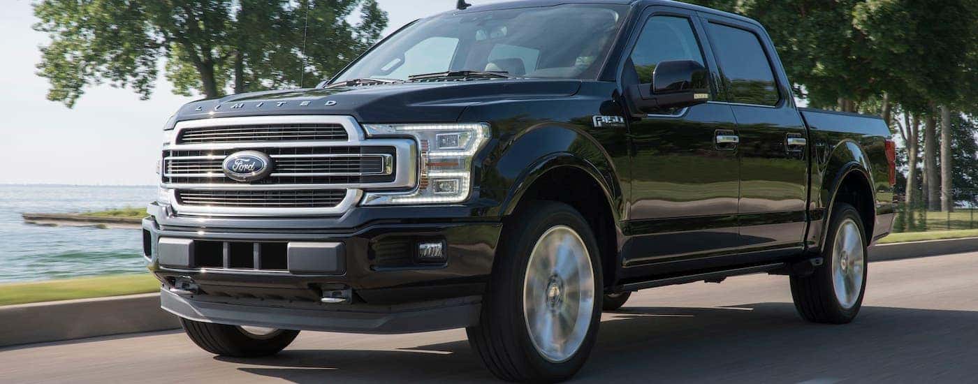 A popular used Ford truck for sale, a black 2018 Ford F-150 Limited, is driving along a lake.