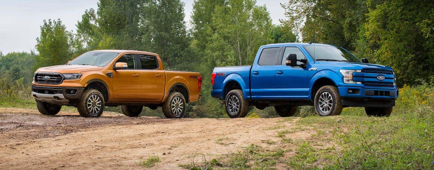 An orange 2019 Ford Ranger and a blue F-150 are parked on a dirt trail.