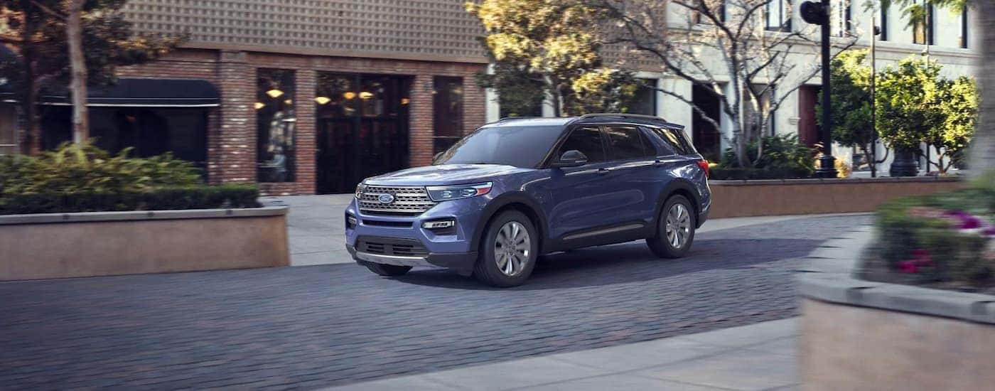 A pale blue 2021 Ford Explorer is shown driving past blurred brick buildings.