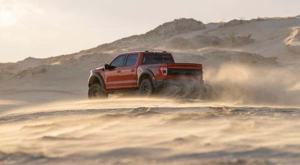 A red 2021 Ford Raptor is driving away on a sand dune.