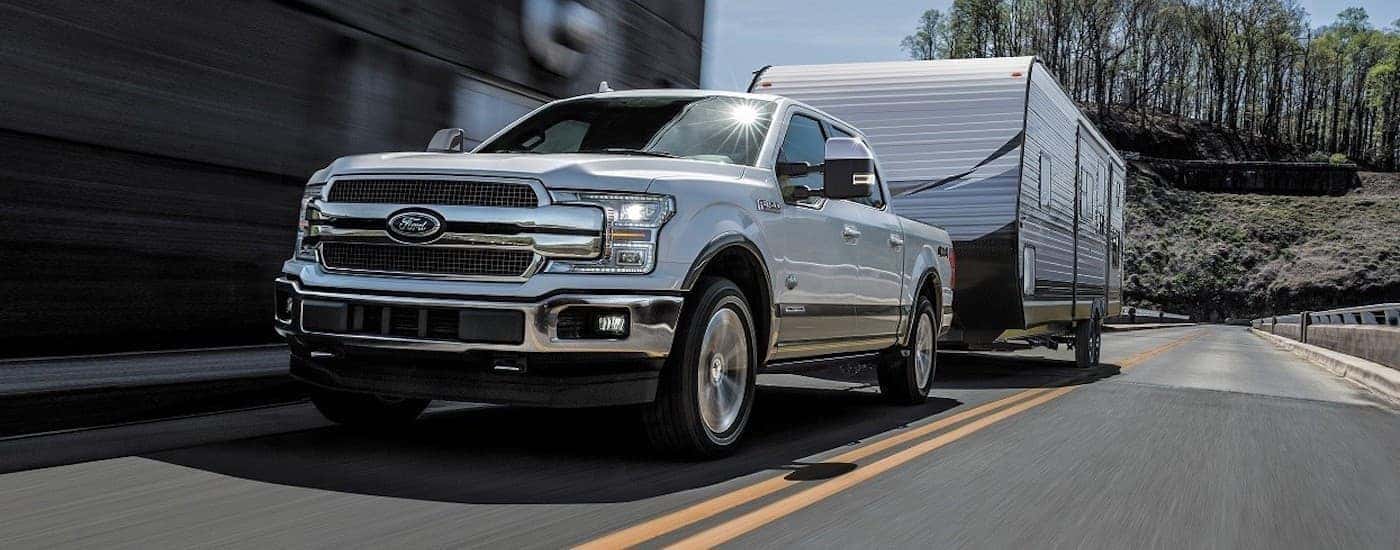 A silver 2018 Ford F-150 is shown towing a camper down an open road after looking at Cincinnati used cars.