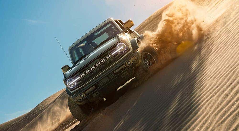 A gray 2021 Ford Bronco 4-door is shown at an angle driving on a sand dune.