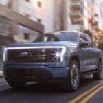 A blue 2022 Ford Lightning is shown driving through a city after leaving a Ford Lightning dealership.