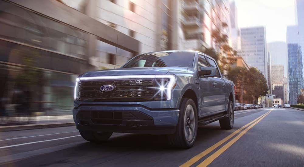 A blue 2022 Ford Lightning is shown driving through a city after leaving a Ford Lightning dealership.