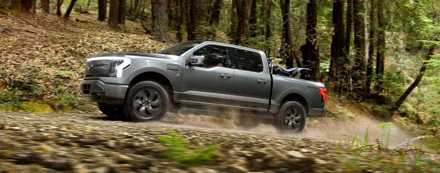 A grey 2022 Ford Lightning is shown off-roading in a forest.