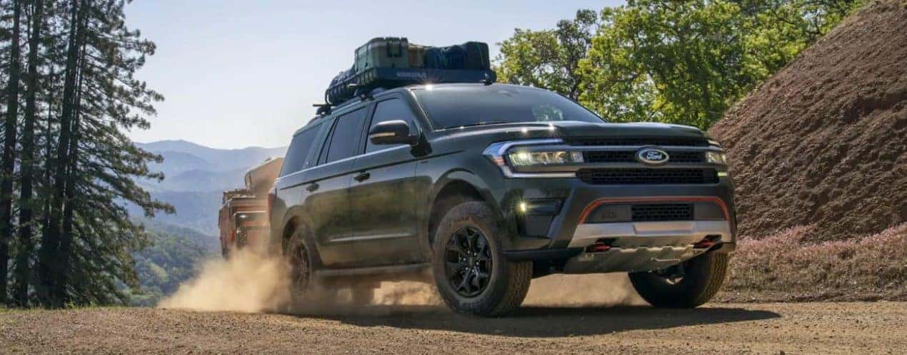 A green 2022 Ford Expedition is shown towing a trailer on a dirt road in the mountains.