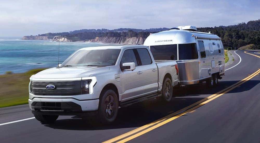 A silver 2022 Ford F-150 Lightning is shown from the front at an angle while towing a camper.