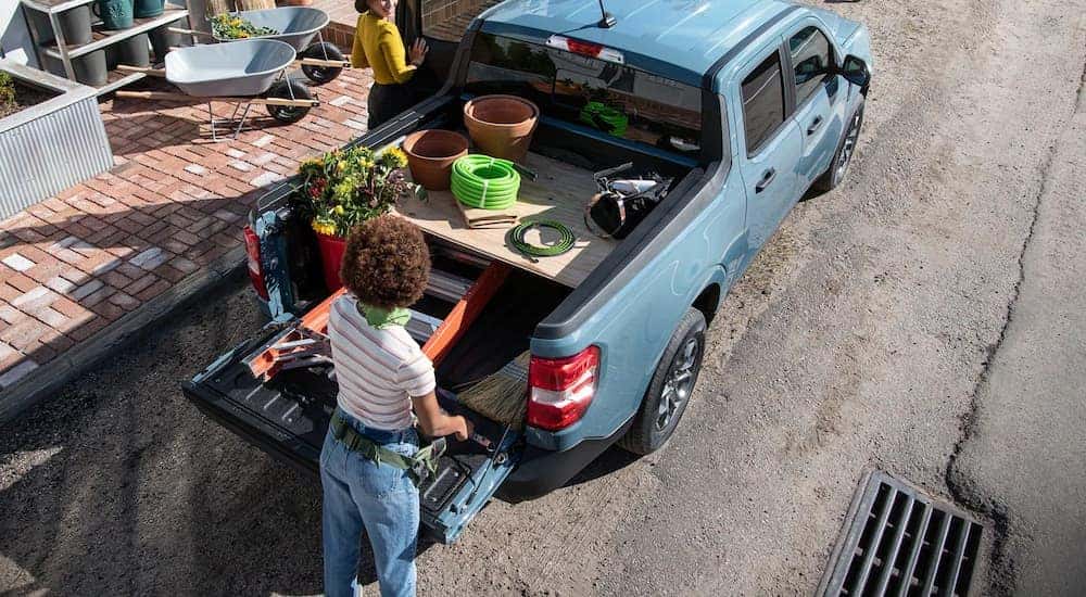 A woman is shown putting supplies into the bed of a blue 2022 Ford Maverick.