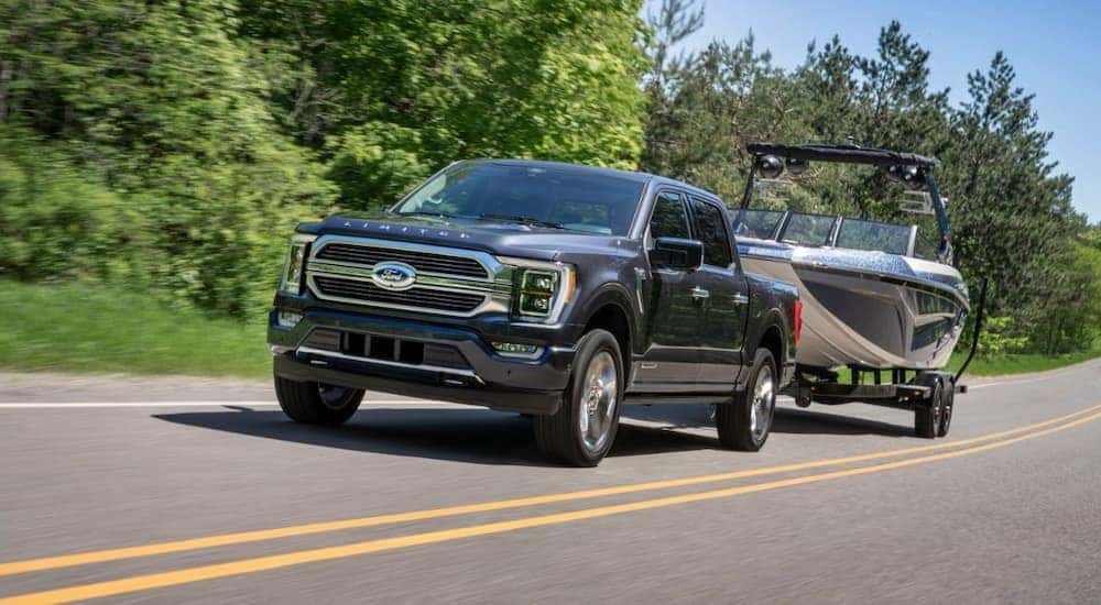 A black 2021 Ford F-150 Limited Hybrid is shown towing a boat after leaving a certified pre-owned Ford dealer.