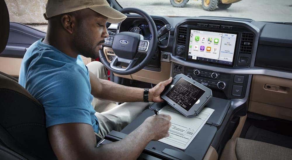 A man is shown doing paperwork in the front seat of a 2021 Ford F-150.