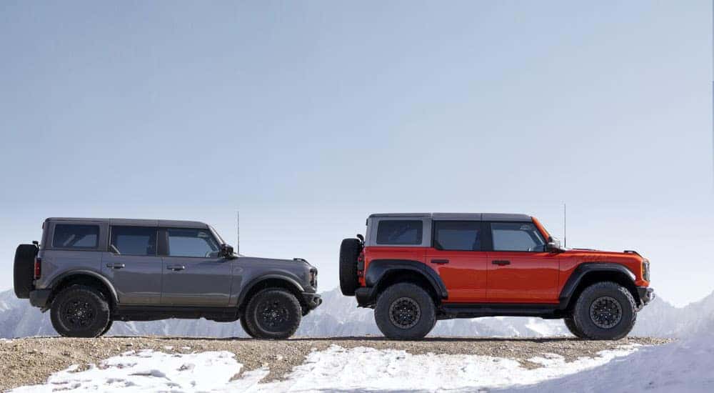 A grey 2022 Ford Bronco Wildtrak and an orange Bronco Raptor are shown from the side near mountains.