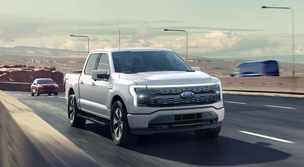 A grey 2022 Ford F-150 Lightning is shown from the front driving on an open road.