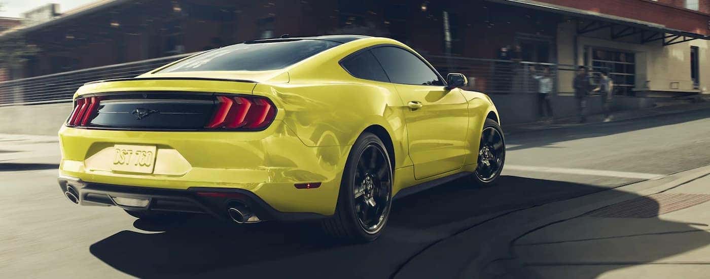 A yellow 2021 Ford Mustang is shown driving on a city street.