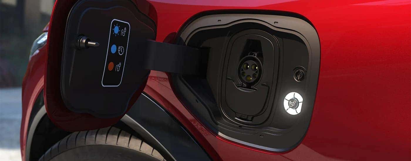 A close up shows the charging port on a red 2022 Ford Mustang Mach-E.