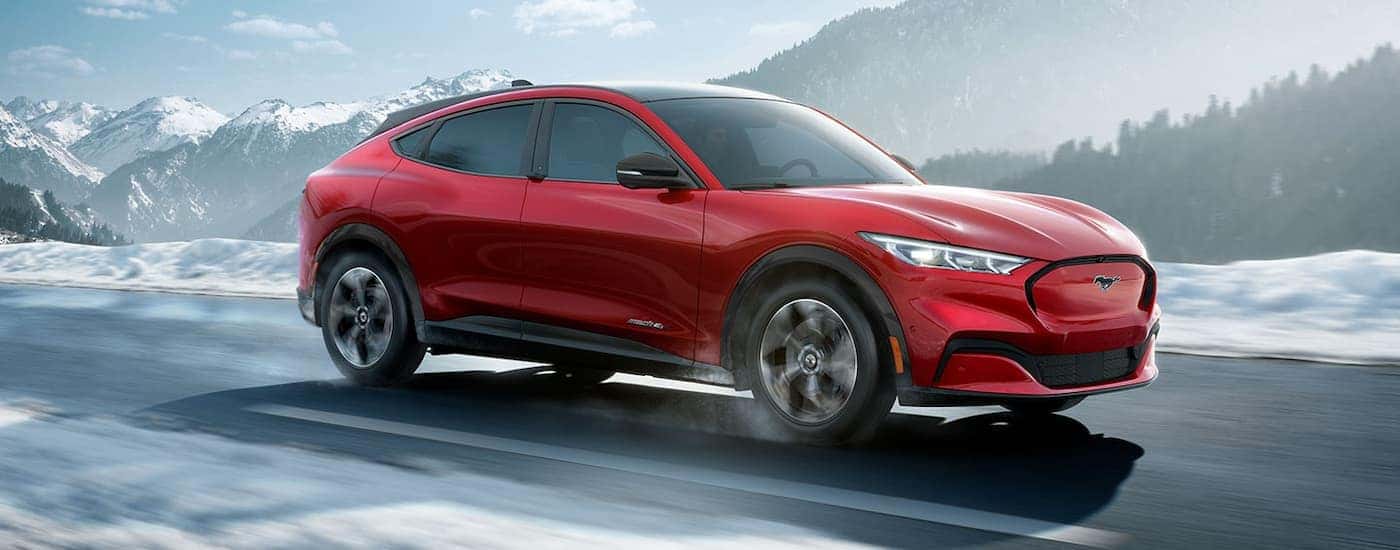 A red 2023 Ford Mustang Mach-E is shown driving past snow covered mountains. 