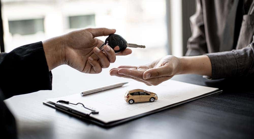 A customer handing a car key to a car salesman after selling their car
