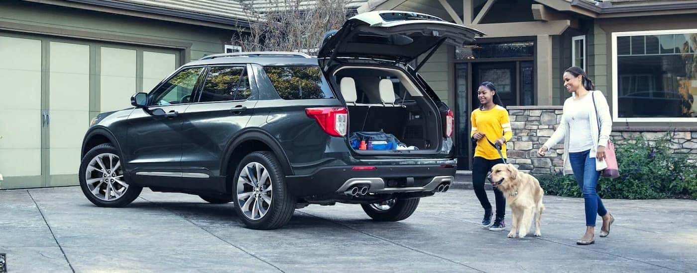A mother, daughter, and their dog approach a grey 2022 Ford Explorer in a driveway with the trunk open.