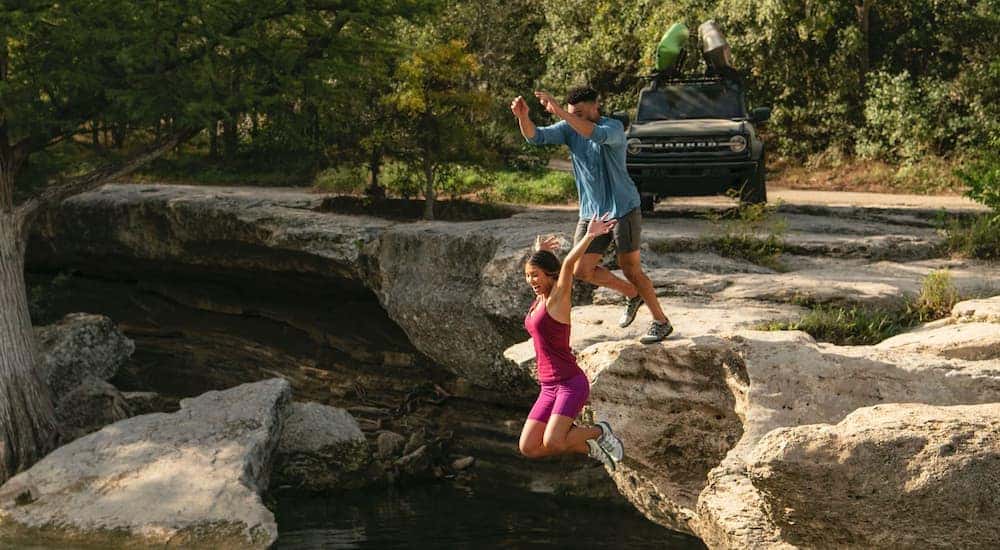 People cliff diving near a green 2023 Ford Bronco with kayaks on the roof