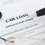 Person filling out a car loan application next to a calculator