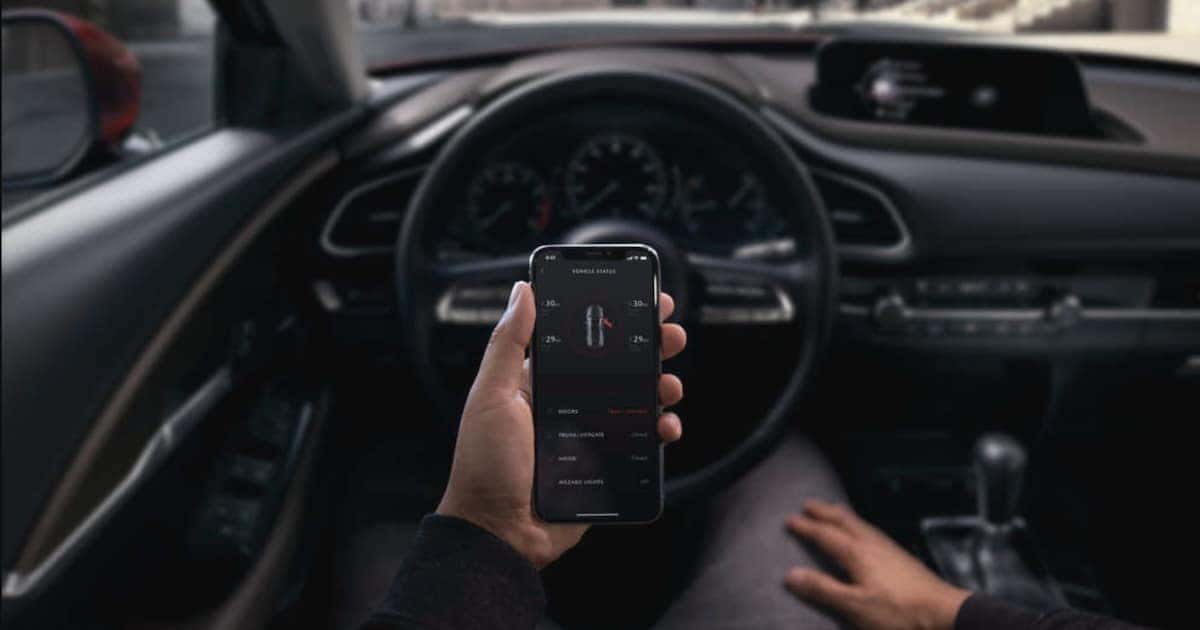 2024 Mazda3 sedan and a person using the MyMazda app to access Mazda Connected Services on their smartphone