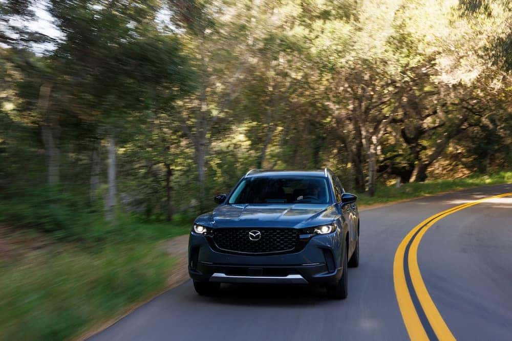 2026 Mazda CX-50 driving on a tree-lined road
