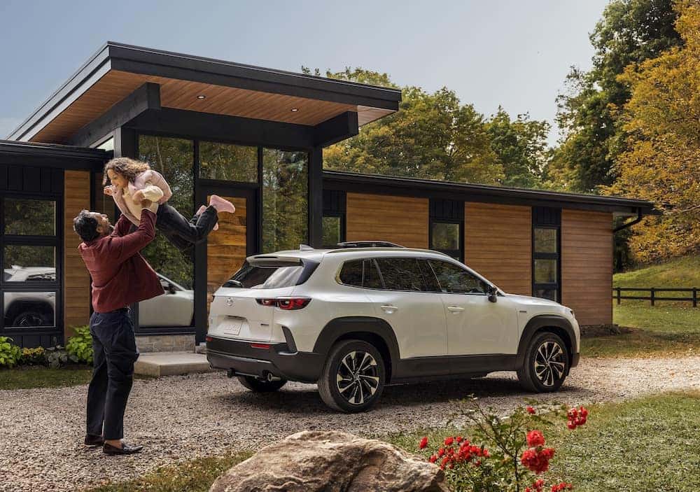 A man with his daughter next to their 2026 Mazda CX-50 Hybrid, one of the safest SUVs available.